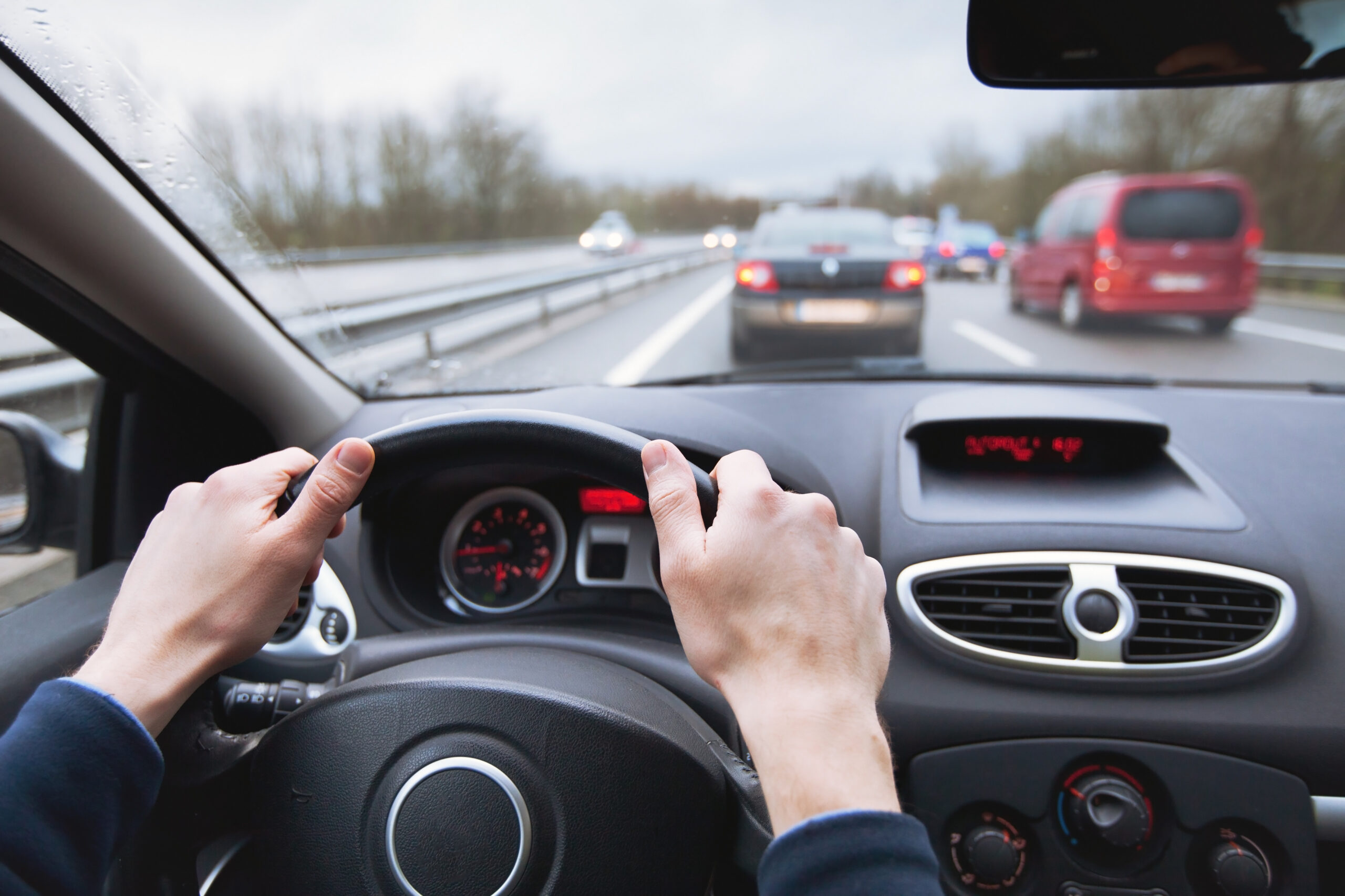 driver's seat perspective of car driving on highway with hands on the wheel